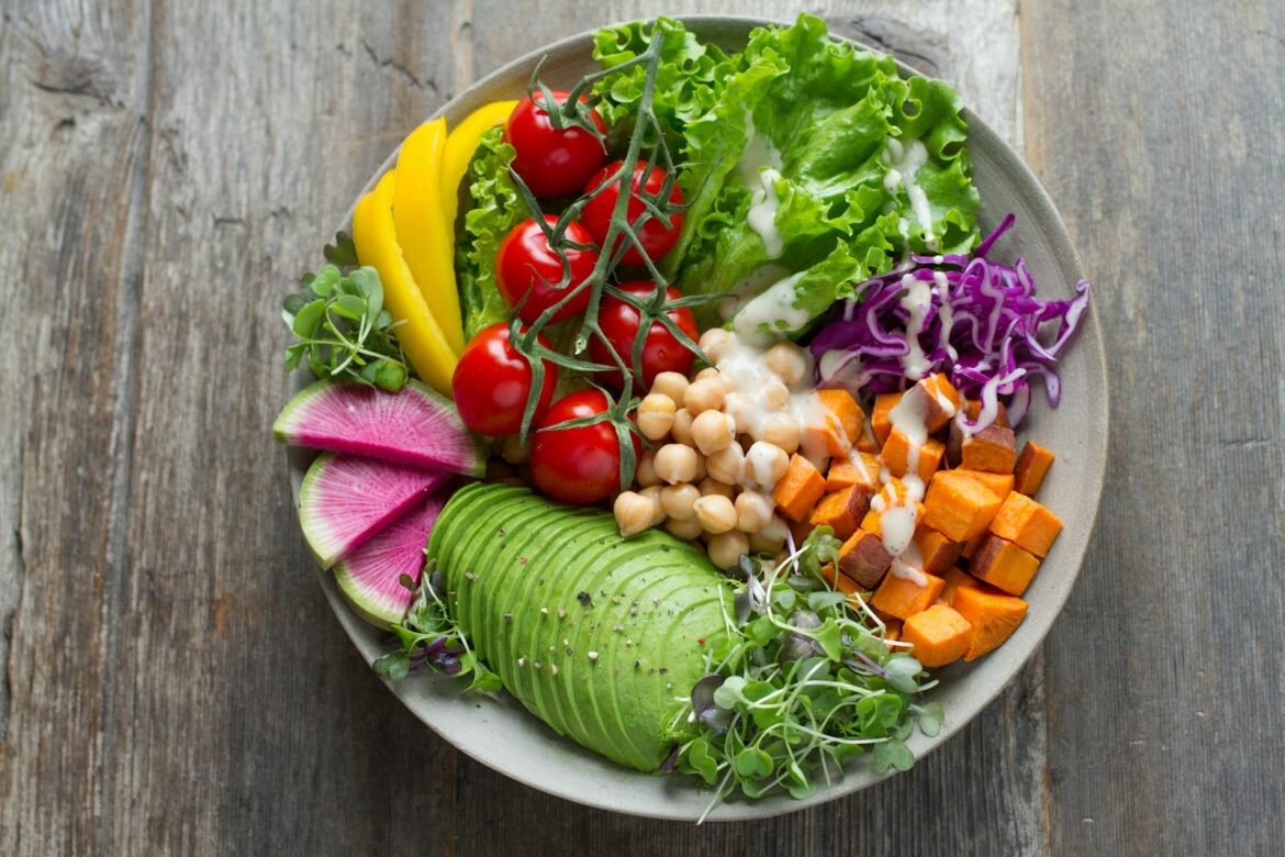 Bowl of fresh vegetable salad with greens tomatoes and seeds on a dark surface