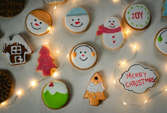Decorated Christmas sugar cookies including snowmen, trees and a Merry Christmas plaque, surrounded by fairy lights