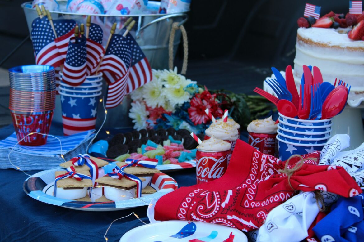 Patriotic dessert table with berry cake, smores and cookies beside small American flags