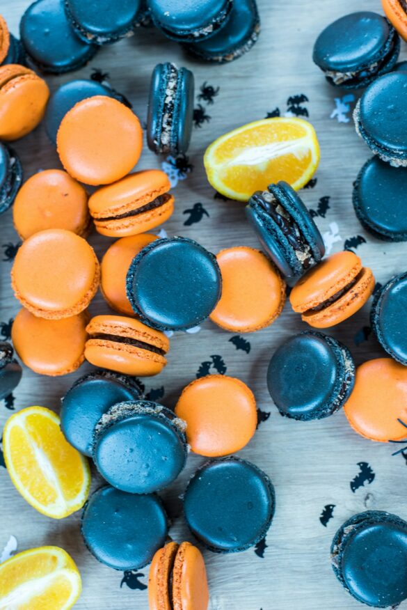 Orange and black Halloween macarons scattered with bat and ghost confetti and orange slices
