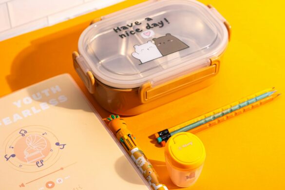 Bento style lunch box with notebook and pencils on a bright yellow table