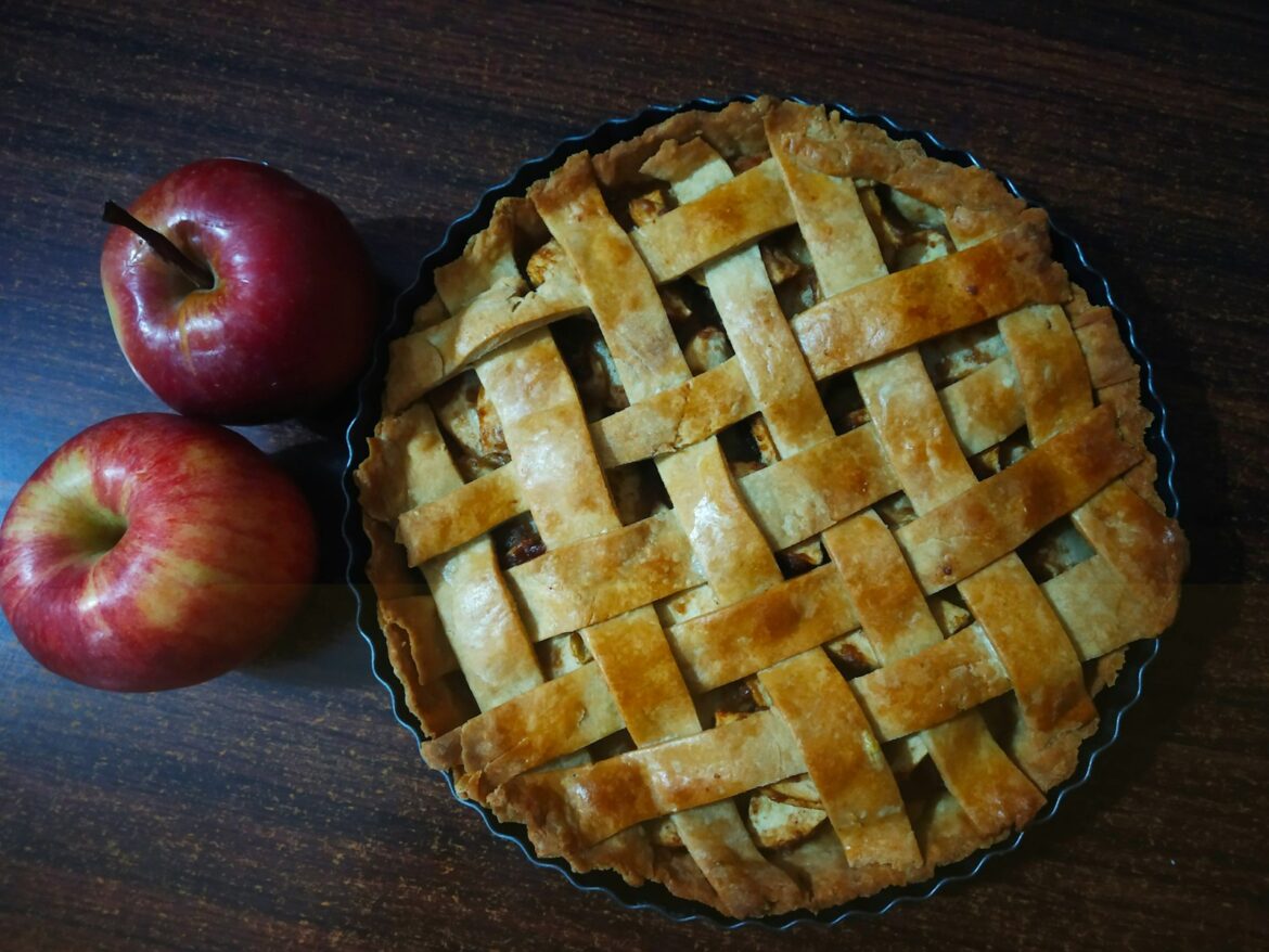 Lattice topped apple pie in a tart tin beside two red apples
