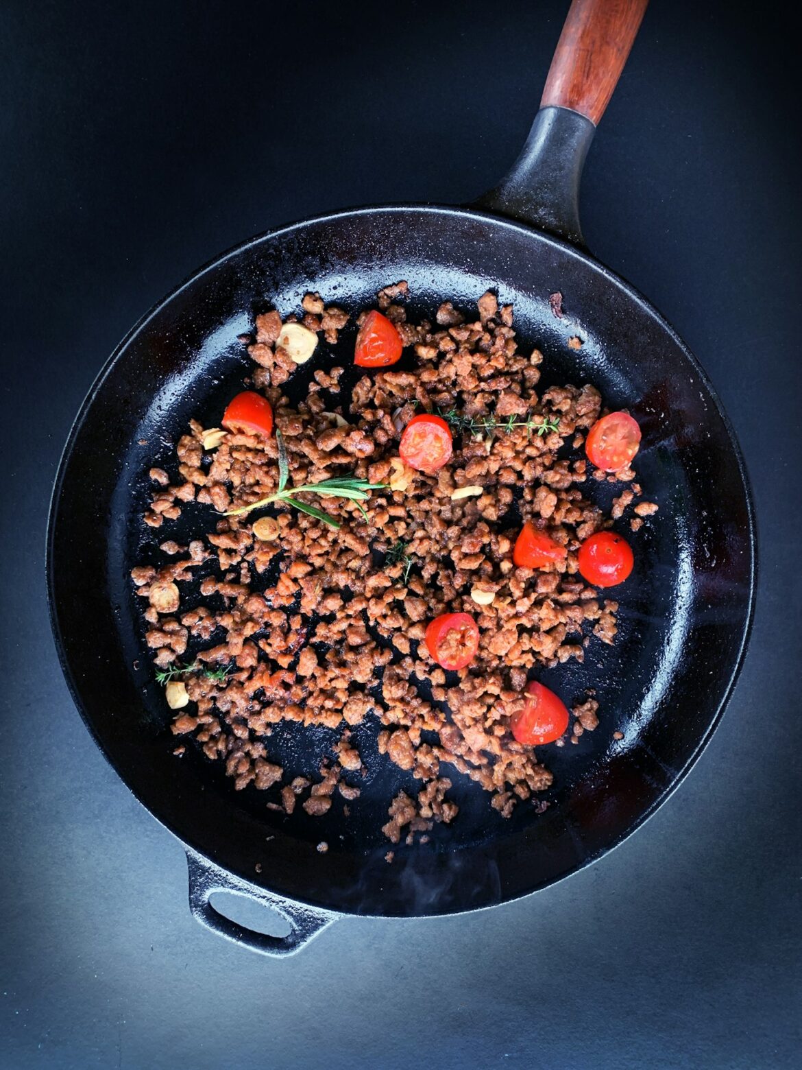 Browned ground beef with cherry tomatoes and fresh herbs in a cast iron skillet