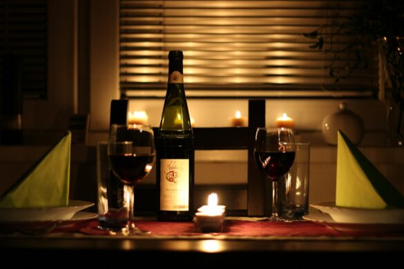 A candlelit table set for two with red wine poured and a lit tealight between the places