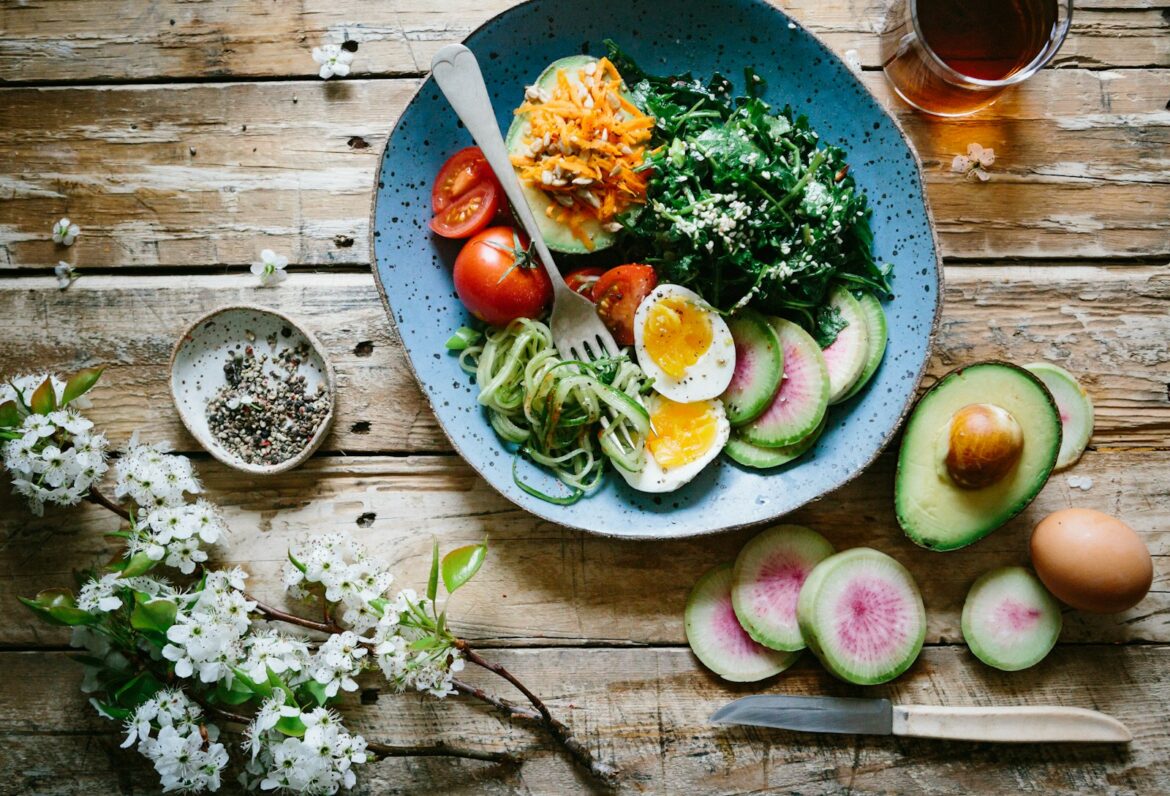 Bowl of soft boiled egg, avocado, tomato, greens and courgette noodles on a wooden table