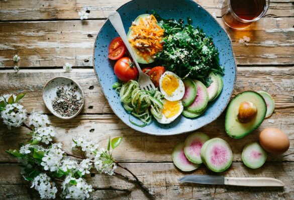 Bowl of soft boiled egg, avocado, tomato, greens and courgette noodles on a wooden table