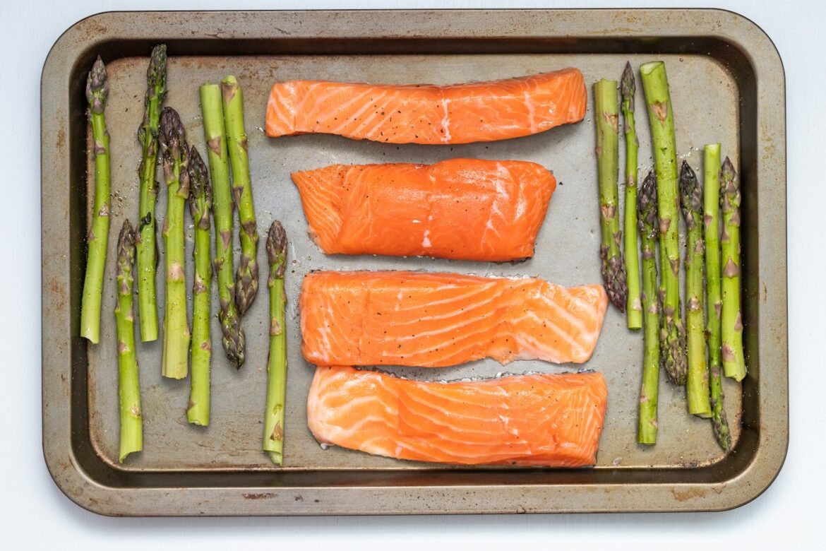 Four salmon fillets and fresh asparagus spears arranged on a sheet pan ready for the oven