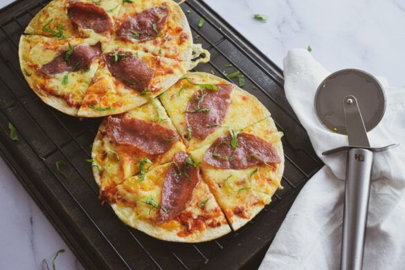 Two crispy personal pizzas topped with cheese and basil, cooling on a wire rack beside a pizza cutter