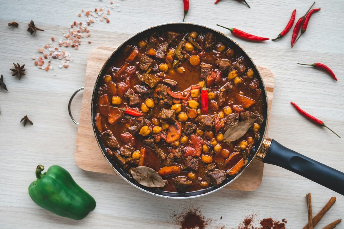 A hearty slow cooked beef and vegetable stew in a pan, surrounded by fresh peppers and spices