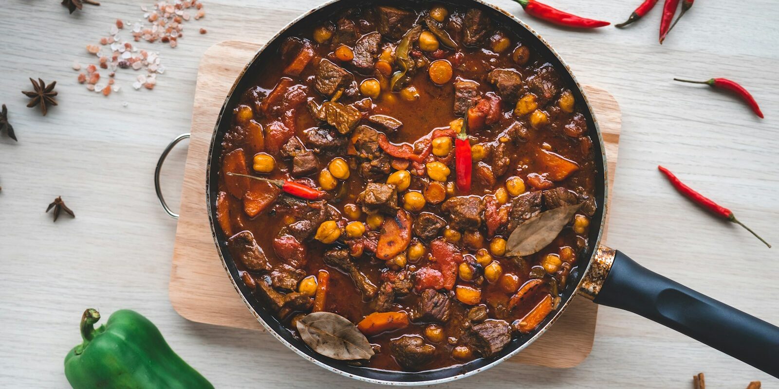 A hearty slow cooked beef and vegetable stew in a pan, surrounded by fresh peppers and spices