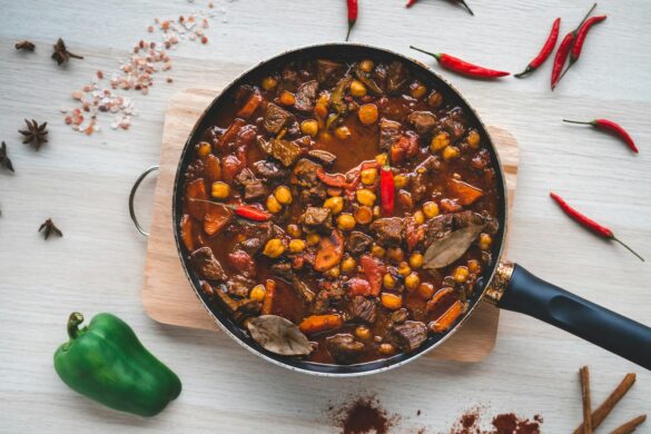 A hearty slow cooked beef and vegetable stew in a pan, surrounded by fresh peppers and spices