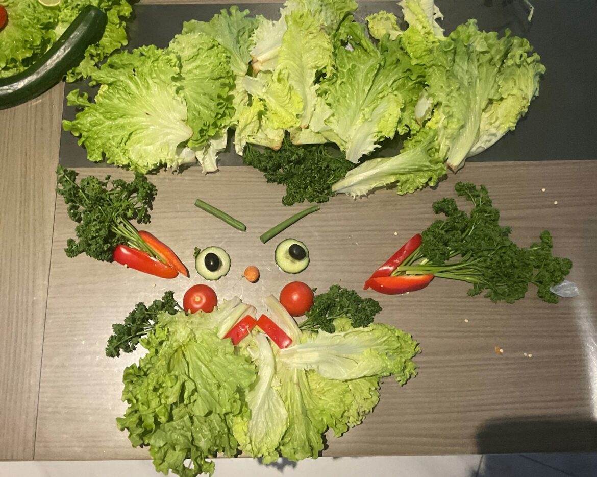 Face made from lettuce peppers tomatoes and parsley arranged on a table