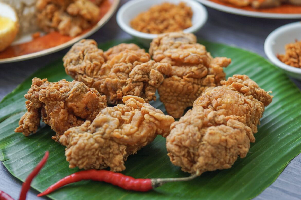 Golden crispy fried chicken pieces served on a green banana leaf with red chillies