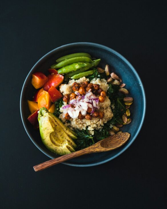 A vegan dinner bowl with quinoa, roasted chickpeas, kale, avocado, tomatoes and sugar snap peas
