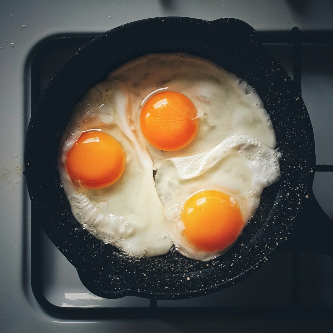 Three eggs frying in a black pan on a hob