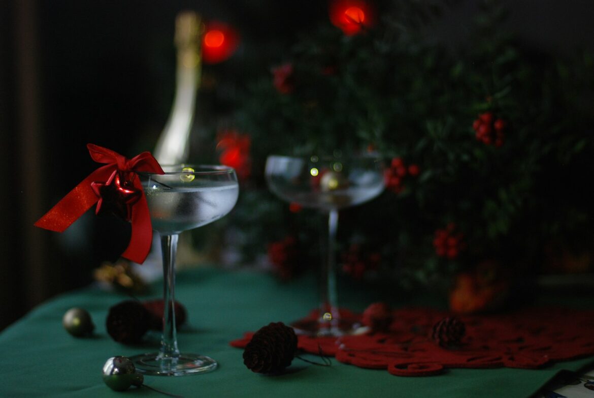 Two coupe cocktail glasses tied with a red ribbon beside a bottle and a decorated Christmas tree