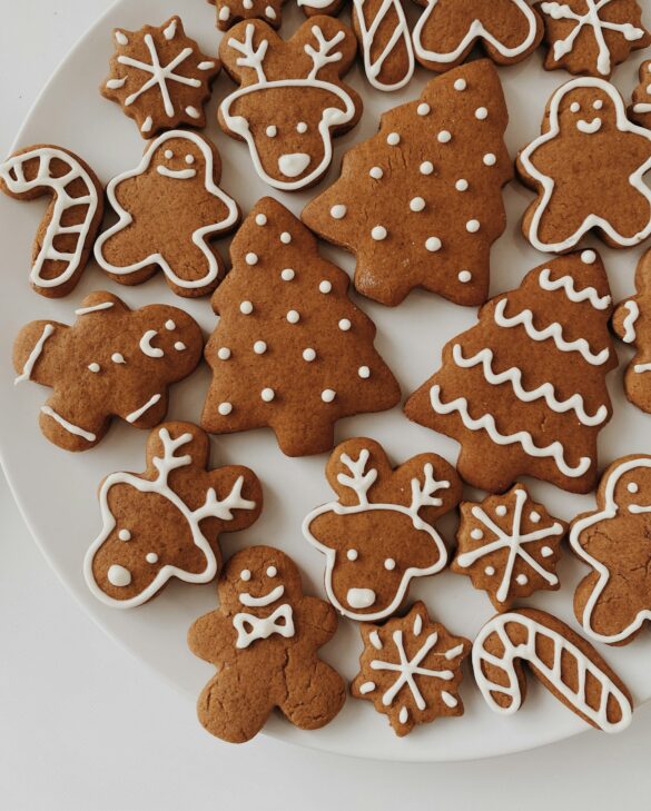 A white plate of decorated gingerbread Christmas cookies including trees, reindeer, snowflakes and candy canes