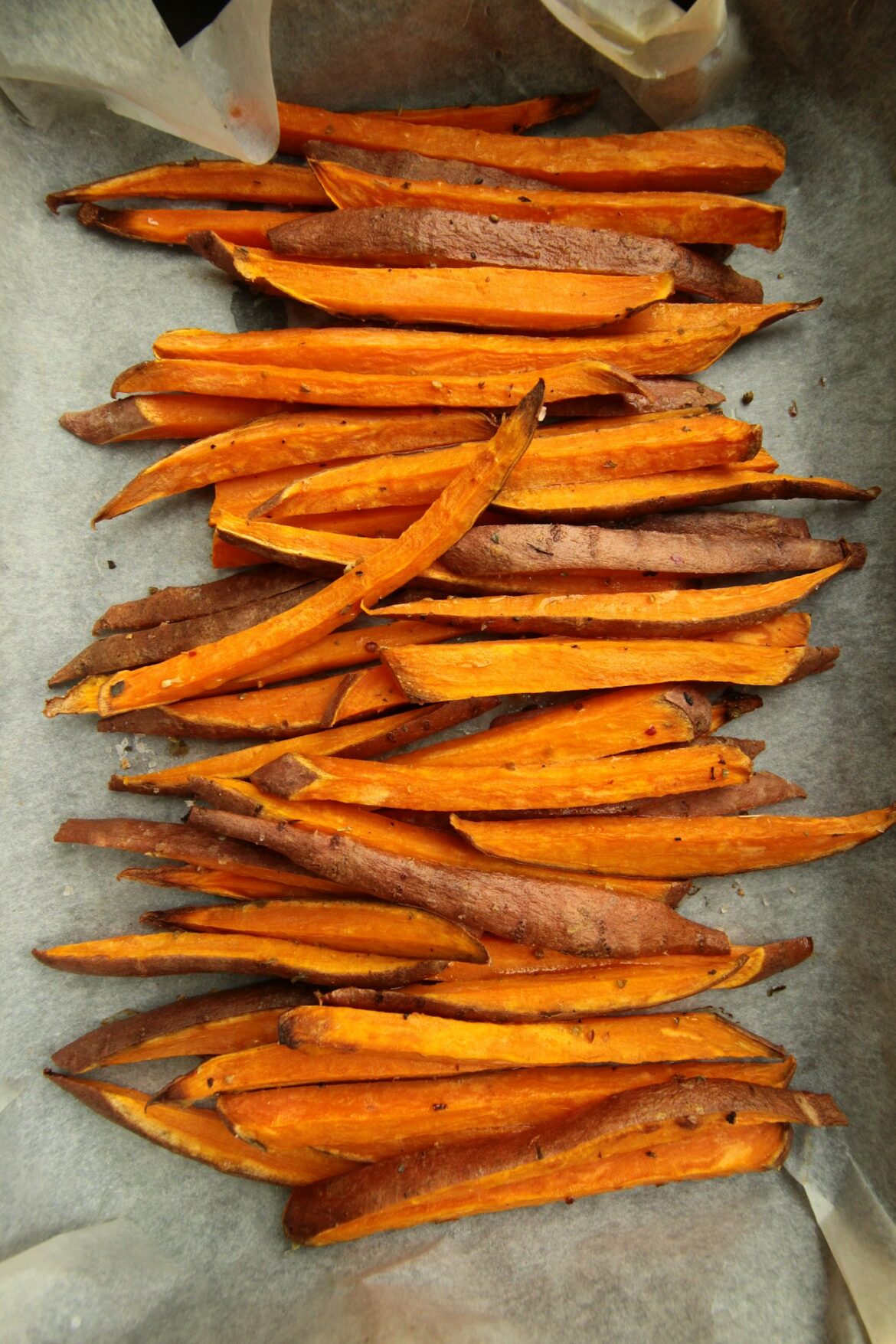 Crispy seasoned sweet potato fries laid out on baking parchment