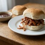 Crockpot pulled pork piled onto a soft white roll, glossy with barbecue sauce