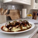 Slow cooker short ribs in a dark gravy over mashed potatoes on a white platter