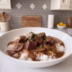 Crockpot beef tips in a brown mushroom gravy over white rice in a wide white bowl