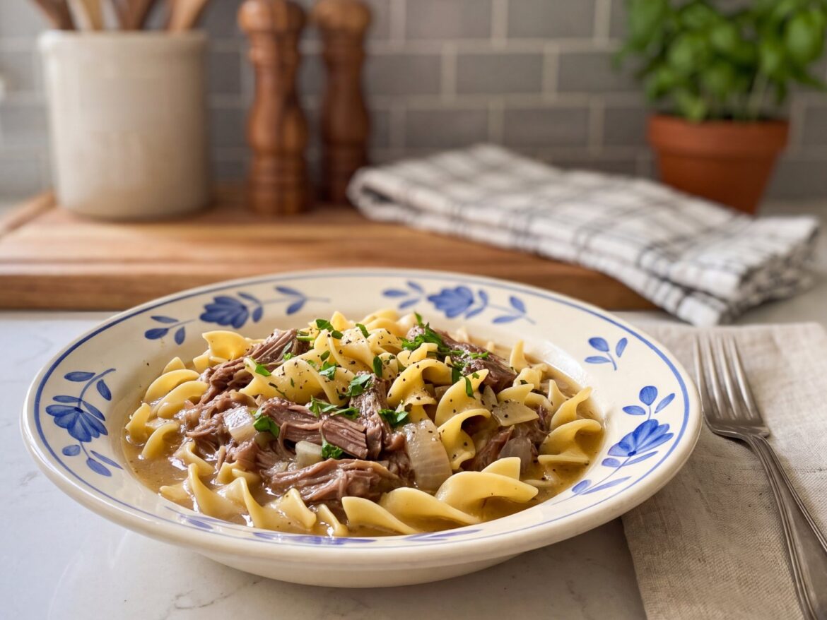 Crockpot beef and noodles with shredded beef and egg noodles in a cream bowl with a blue floral rim