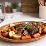 Crockpot chuck roast in tender pieces with red potatoes, carrots and gravy on a brown stoneware platter