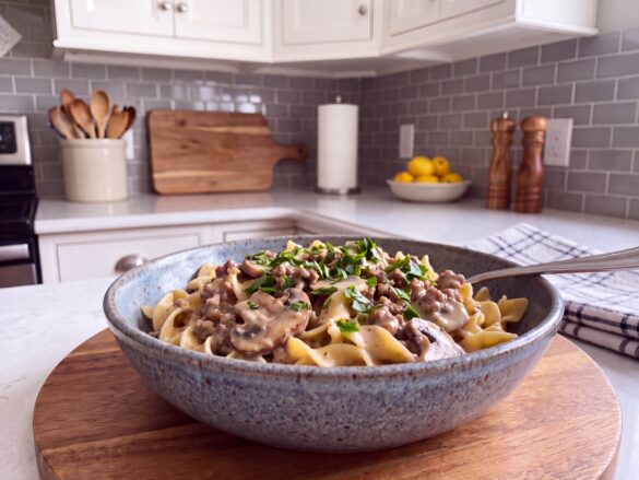 Ground beef stroganoff with egg noodles and mushrooms in a creamy sauce in a speckled blue stoneware bowl