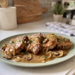 Smothered crock pot pork chops in onion and mushroom gravy with parsley on a sage green platter